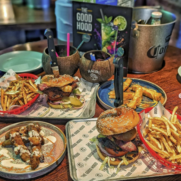 Good Hood table of food featuring Burgers, chicken wings, fries and cocktails